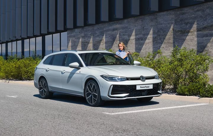 Una Volkswagen Passat bianca riposa in un ambiente urbano moderno, incarnando il motivo per cui Perchè Sceglierci. Una persona è in piedi accanto all'auto, sullo sfondo di verde e un elegante edificio.