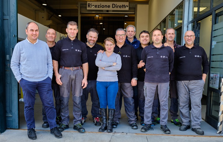 Un gruppo di undici persone, alcune in camicia nera e altre in jeans e abbigliamento casual, sono sorridenti davanti all'ingresso di un edificio con la scritta "Ricezione Diretta". Questa scena accogliente d'avanti a Caltabiano Auto suggerisce un'atmosfera amichevole sul posto di lavoro.